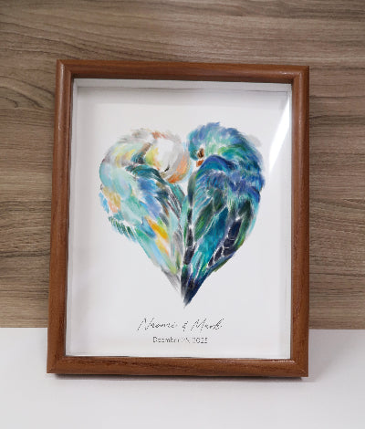 Framed artwork of two birds in a heart shape with personalized text on a wooden surface.